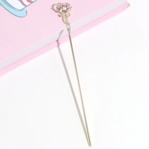 Detailed shot of golden metal hair pin with pink heart gemstone on a book background