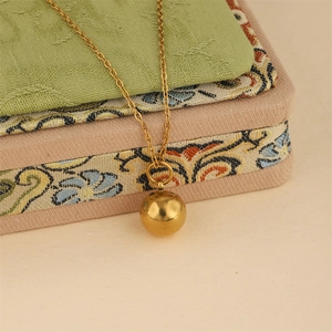 Minimalist 18K gold ball pendant necklace displayed on a vintage embroidered jewelry box