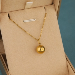 Polished 18K gold ball pendant necklace on a beige velvet jewelry display box