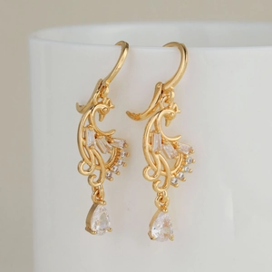 Boucles d'oreilles pendantes phénix dorées avec zircons sertis sur une tasse céramique