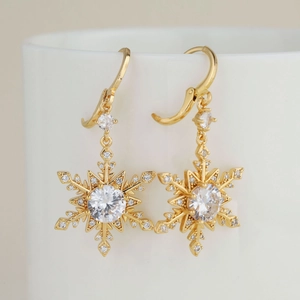 Élégantes boucles d'oreilles flocon de neige dorées avec zircones suspendues sur une tasse
