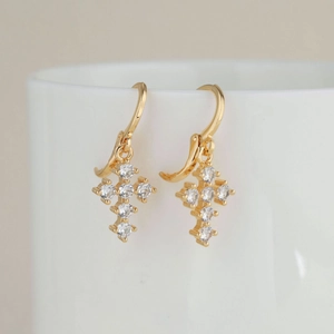 Goldene Kreuzohrringe mit Zirkonia-Steinen, hängend an einem weißen Keramikbecher