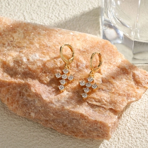 Goldene Kreuz-Ohrringe mit Zirkonia-Steinen auf einem natürlichen Steinsockel