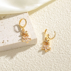 Boucles d'oreilles fleurs dorées avec cristaux blancs sur fond de pierre de luxe
