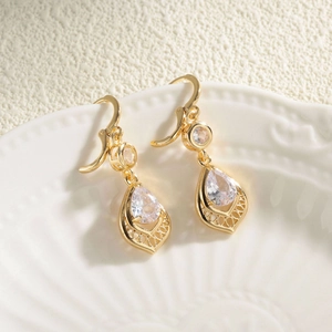 Elegant gold pear-shaped drop earrings with clear zircon stones on a white ceramic plate