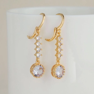Boucles d'oreilles pendantes dorées avec zircons géométriques sur une tasse en céramique