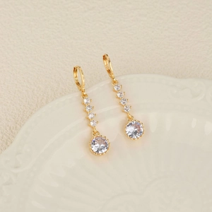 Boucles d'oreilles pendantes dorées avec zircones sur une assiette en céramique vintage