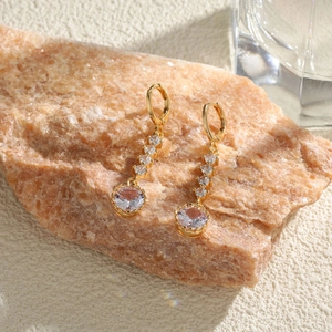 Longues boucles d'oreilles dorées avec oxydes de zirconium sur fond de pierre naturelle