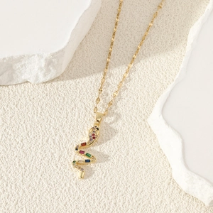 Elegant gold snake pendant necklace with multi-color zircons on a white stone surface