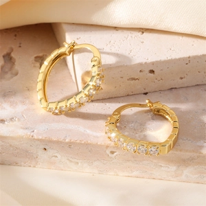 Elegant gold-plated oval hoop earrings with clear cubic zirconia on stone background
