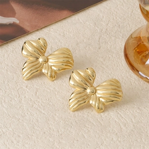Polished 18K gold bow-shaped titanium steel stud earrings on a textured beige surface