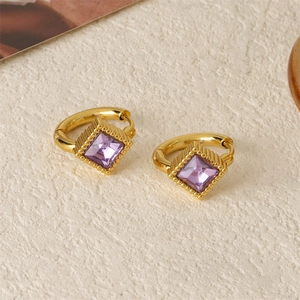 Golden rhombic zircon hoop earrings with purple square gemstones on a textured surface