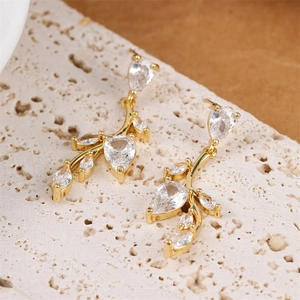 Elegant gold leaf branch earrings with sparkling zircons displayed on natural stone