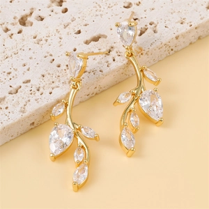 Elegant gold willow leaf earrings with cubic zirconia tassels on a textured stone base