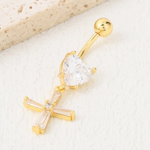 Piercing de nombril doré avec pendentif cœur et croix sur fond de pierre blanche