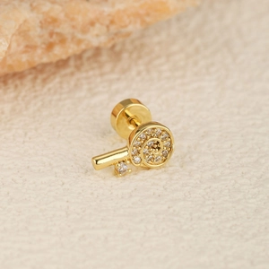 Detailed close-up of a golden key-shaped earring with sparkling cubic zirconia on beige texture