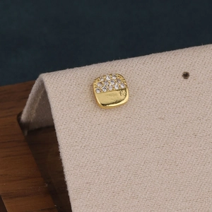 Gros plan d'un clou d'oreille carré doré serti de zircons sur un support beige