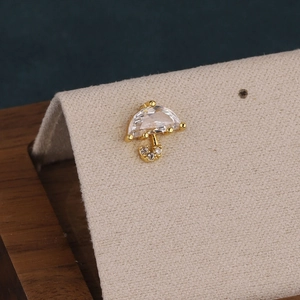 Detailed view of a gold umbrella earring with clear cubic zirconia on a beige stand