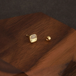 Photo macro d'une boucle d'oreille carrée dorée avec zircons pavés et surface polie lisse