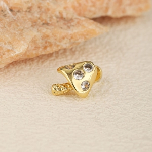 Gold-plated mushroom tragus stud with sparkling zircons on beige textured background