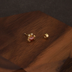 Gros plan sur un clou d'oreille crabe doré serti d'une gemme orange sur bois sombre