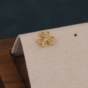 Macro shot of gold floral cartilage stud with sparkling pavé crystals on textured stand