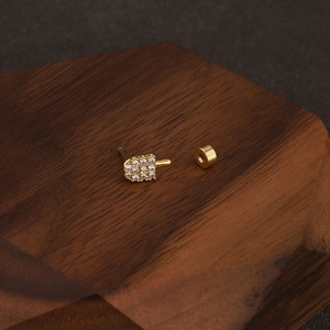 Détail macro de la boucle d'oreille en acier doré forme main avec zircone étincelante
