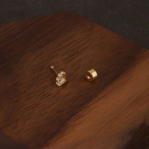 Gros plan d'une puce d'oreille couronne dorée sertie de zircons sur support en bois