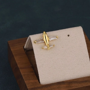 Macro shot of gold airplane stud earring with inlaid crystals on beige velvet stand