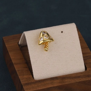 Macro shot of gold mushroom cartilage stud earring with cubic zirconia on wood stand