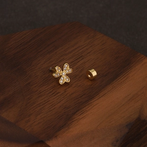 Detailed close-up of golden clover cartilage stud with clear zircons on wood surface