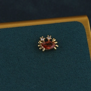Vue détaillée d'une boucle d'oreille crabe dorée avec pierre rouge et diamants blancs