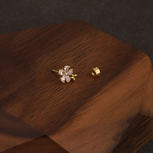 Detailed macro of gold flower cartilage earring with crystal studs on walnut wood stand