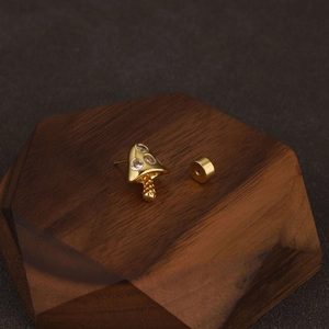 Macro view of gold mushroom ear stud with three sparkling zircons on wooden display