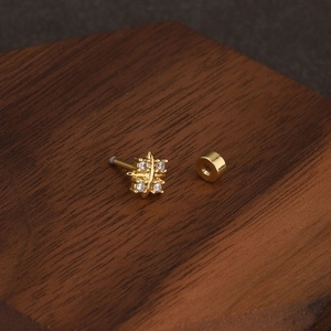Close-up of gold-plated star cartilage piercing with white zircons on wooden background