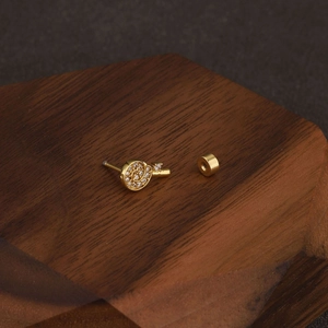 Detailed view of golden spiral cartilage stud with zircon on a dark wooden display