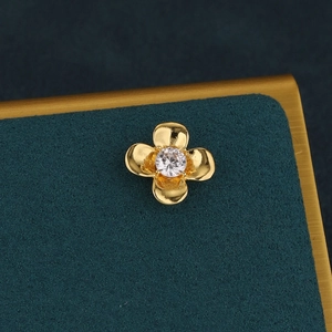 Macro shot of gold floral cartilage stud earring with a white zircon on green velvet