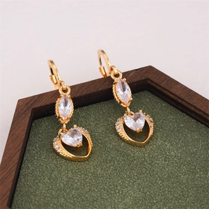 Detailansicht goldener Ohrringe mit Zirkonia und Herzanhängern auf grünem Samttablett