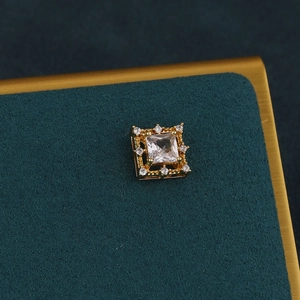 Macro shot of gold square screw-back cartilage stud earring with crystal on velvet