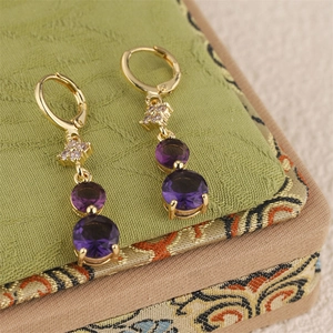 Makroaufnahme goldener Quastenohrringe mit violettem Zirkon und Kreuzblumen-Haken