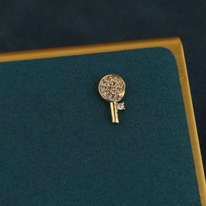 Close-up of golden lollipop cartilage piercing with sparkling paved crystals on dark teal base