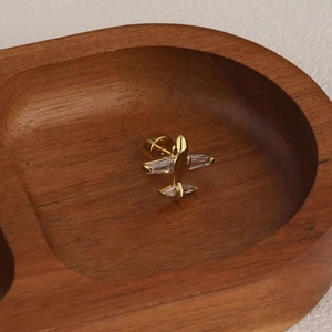 Macro shot of gold airplane cartilage earring with inlaid zircon on dark wood tray