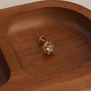 Macro shot of gold starburst cartilage stud with cubic zirconia on wood background