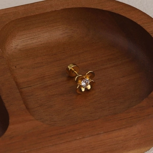 Close-up of golden flower cartilage piercing stud with crystal stone on wooden tray