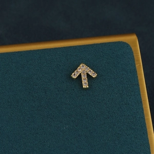 Macro detail of gold arrow cartilage earring with white zircons on teal velvet surface