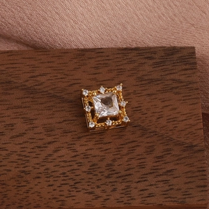 Detailed macro of a square zircon stud with a pavé halo and golden floral metal base