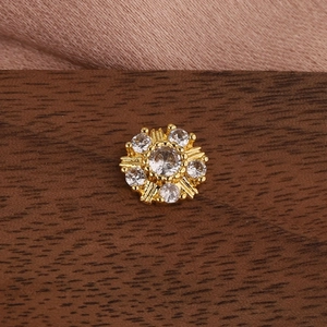 Macro view of gold flower cartilage piercing stud with crystals on silk and wood background