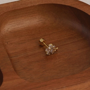 Macro view of flower-shaped golden ear stud with sparkling zircon petals on wood