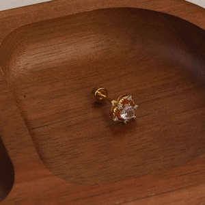 Detail of a golden heart earring with clear zircon and secure screw back on a wood tray