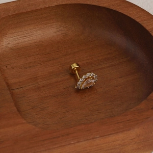 Macro view of gold-plated teardrop cartilage stud with screw back on wood